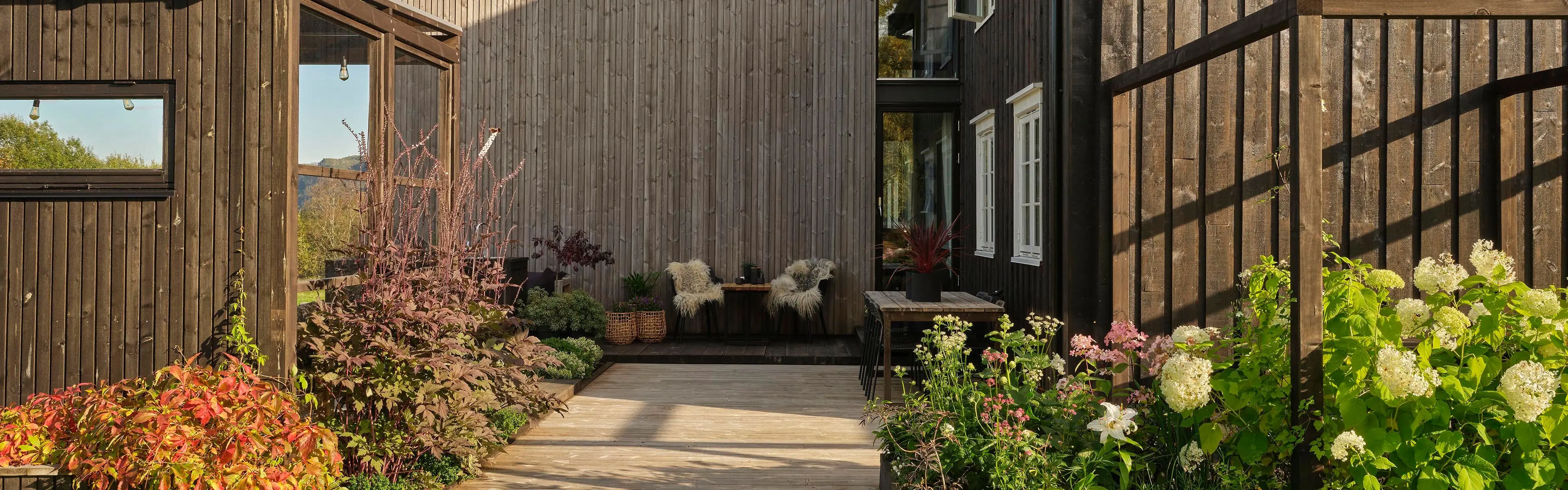 Uteplass og terrasse med pergola og varme farger på terrassebord som er en av årets hagetrender.