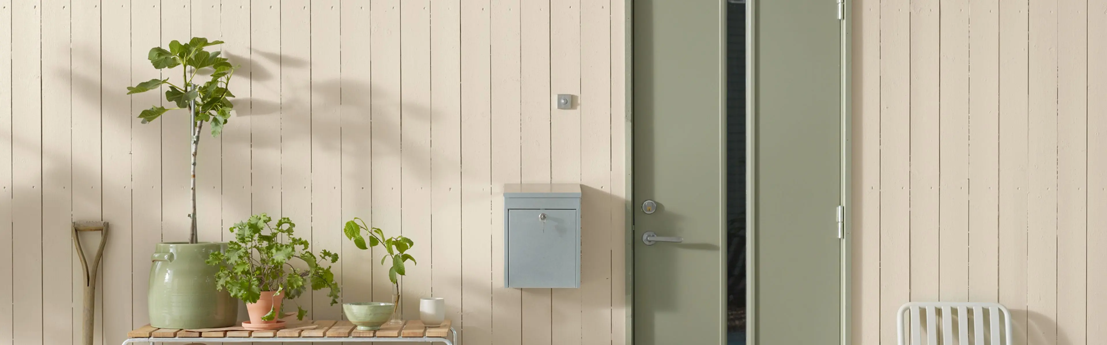 Lysmalt husvegg med plantebenk, postkasse og lysegrønn inngangsdør.