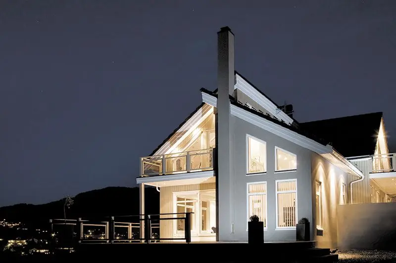 hvitt, moderne hus med store vinduer sett utenfra om kvelden