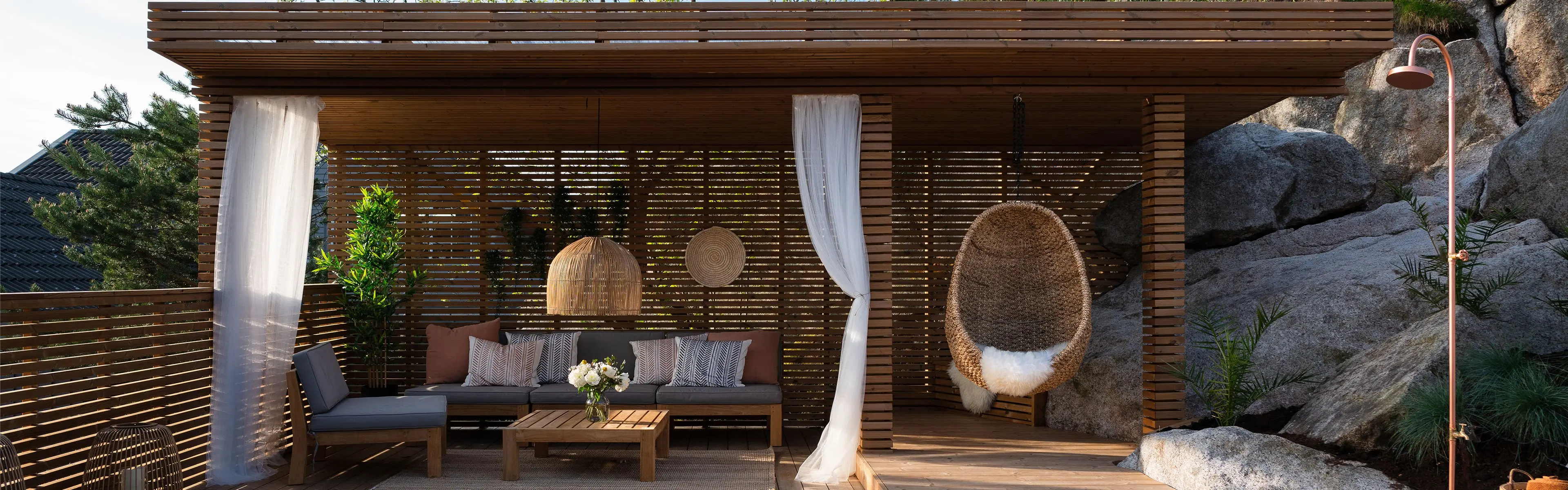 Pergola med tak og vegg fra Moelven. Med sofa, gardiner og hengestol
